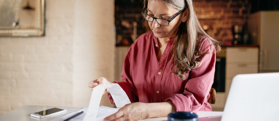 Serious focused middle aged female accountant in eyewear working from home providing outsource bookkeeping service, sitting at table with portable computer, calculating finances, doing paperwork Serious focused middle aged female accountant in eyewear working from home providing outsource bookkeeping service, sitting at table with portable computer, calculating finances, doing paperwork